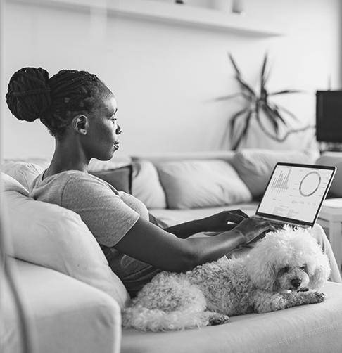 Femme assise sur un canapé à côté de son chien, regardant un écran d’ordinateur portatif montrant des graphiques de placement